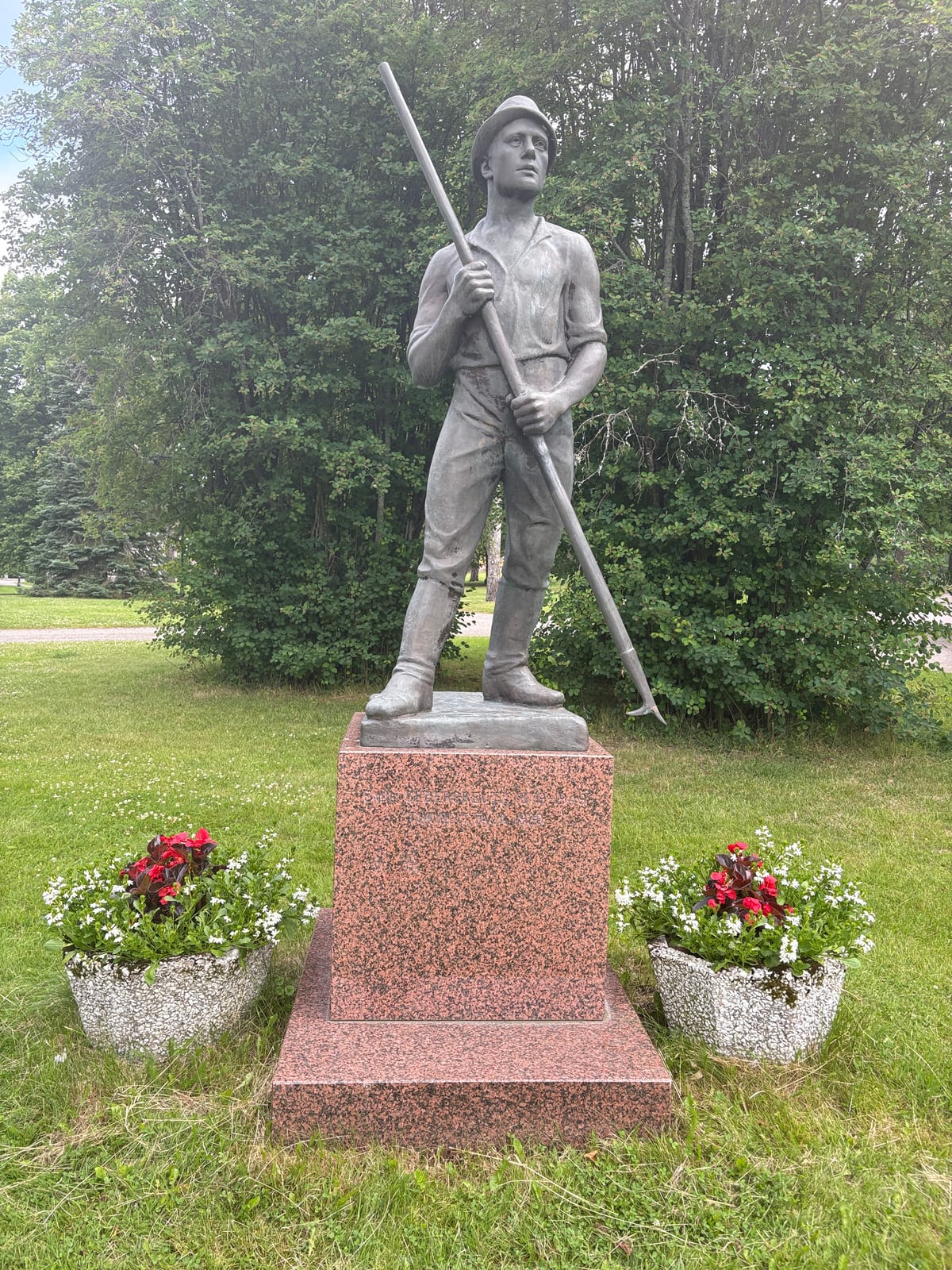 Statue of a log driver (uittomies) on a granite pedestal, pike pole in hand, surrounded by flowers